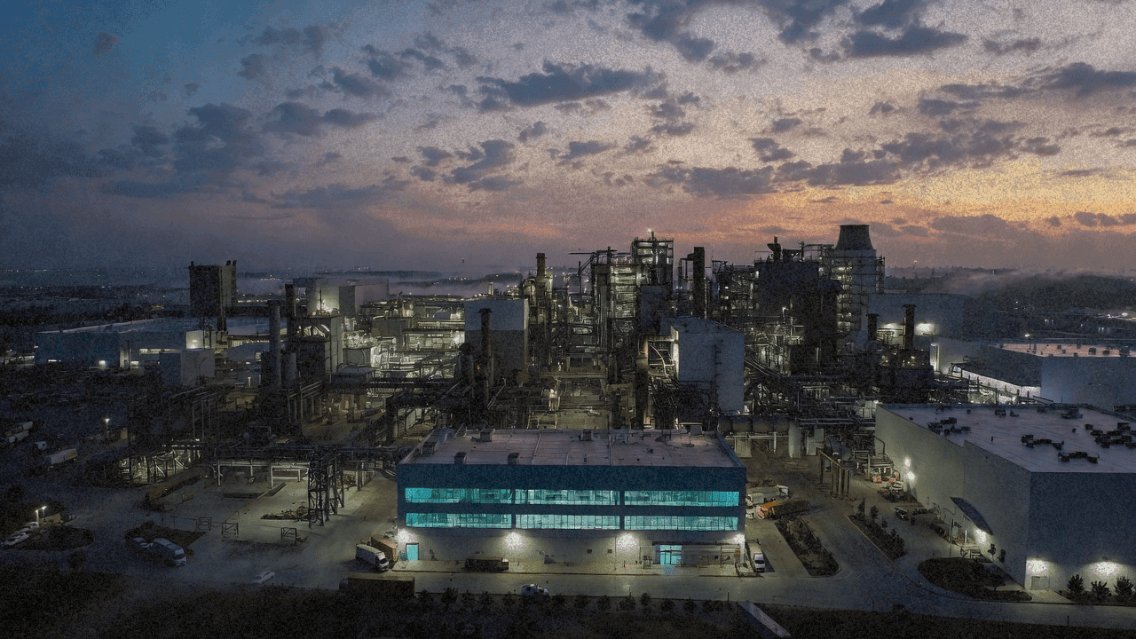 Вид сверху на крупный завод по производству полупроводников в сумерках, через окна видно освещение чистых комнат